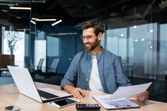 Homme d'affaires m&ucirc;r en chemise faisant de la paperasse, homme travaillant avec des documents, des contrats et des factures assis &agrave; table en utilisant un ordinateur portable au travail, comptable financier avec barbe et lunettes
