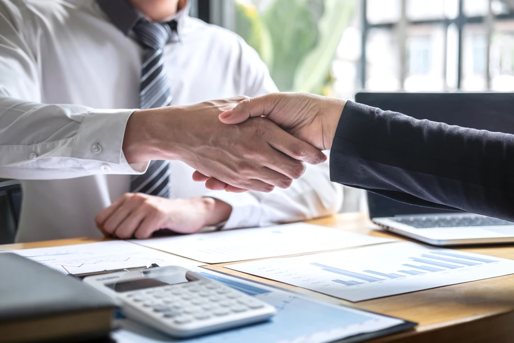 Deux professionnels en costume se serrent la main dans un bureau moderne, scellant un accord commercial