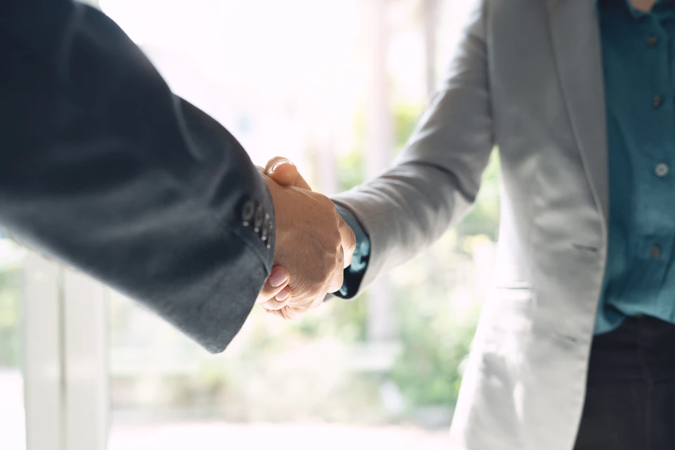Poign&eacute;e de main professionnelle entre deux personnes en costumes sombres dans un environnement de bureau lumineux
