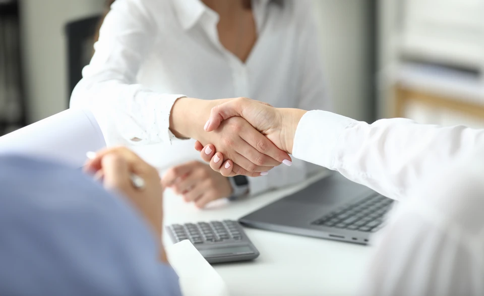Scène de travail collaboratif en bureau avec deux professionnels analysant des documents financiers et graphiques colorés étalés sur table blanche