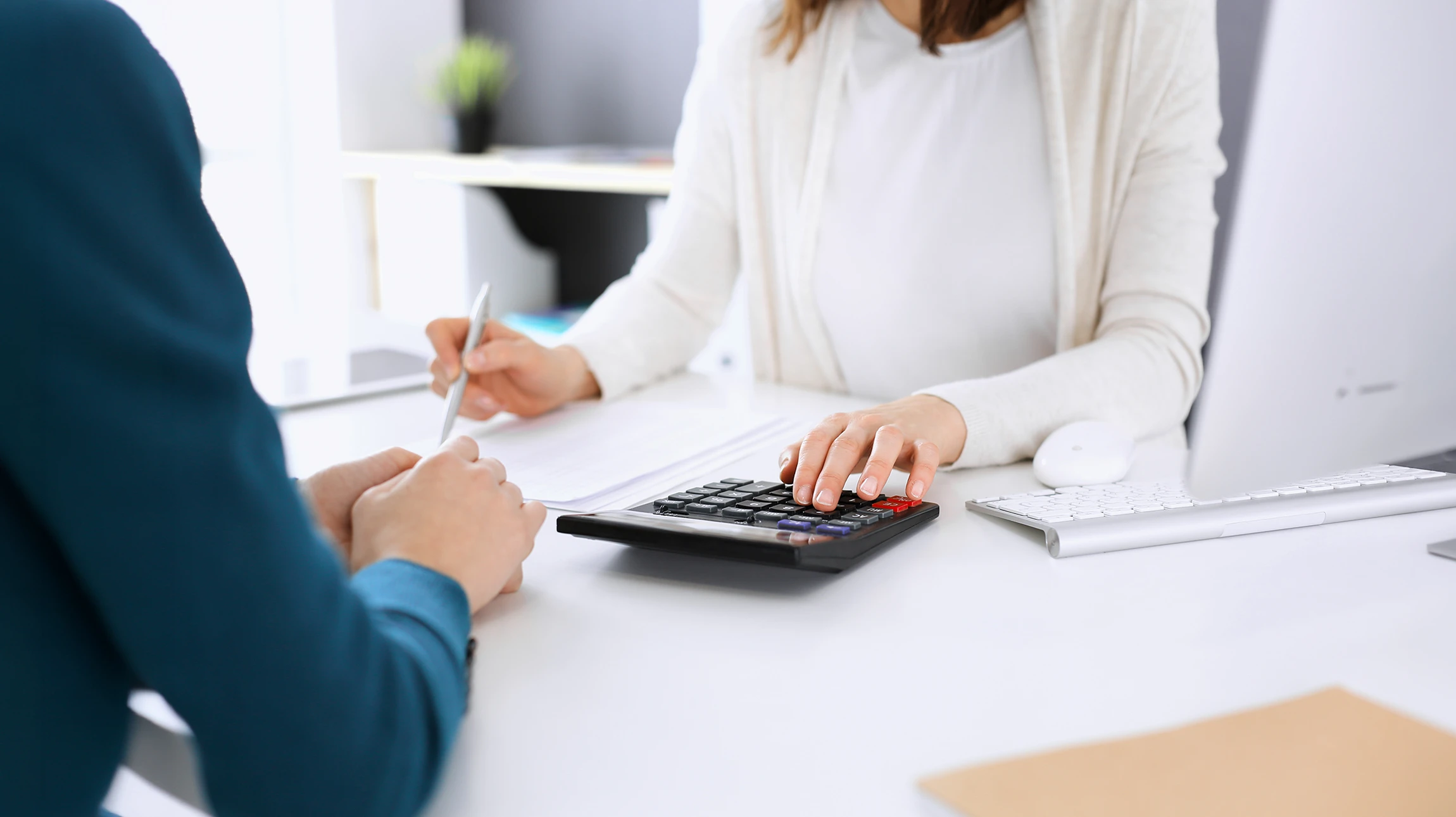 Scène d'intérieur avec mains tenant stylo au-dessus d'un carnet ouvert marqué "BUSINESS PLAN" entouré d'icônes colorées (graphiques, argent, cibles)