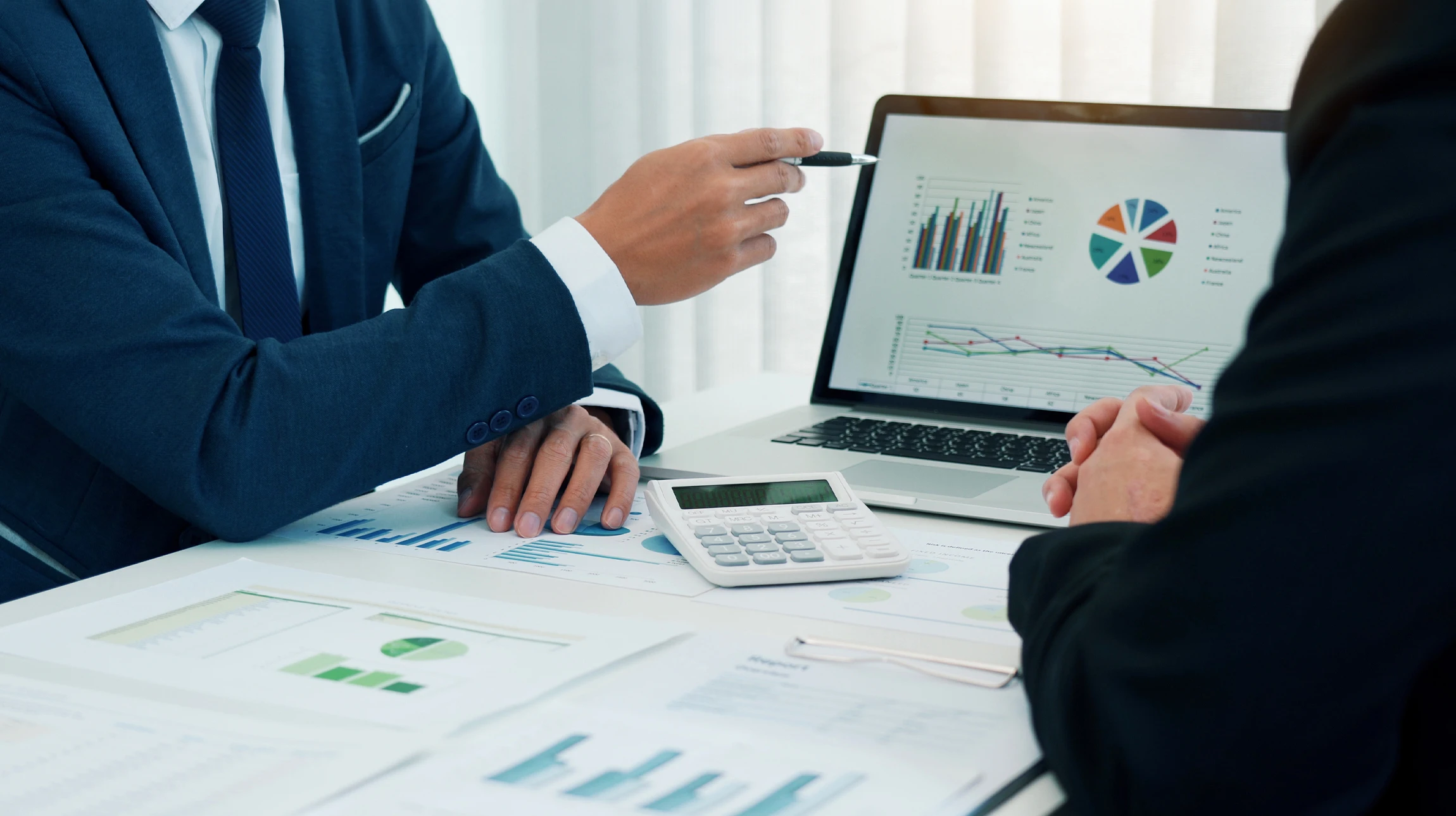 Personne en chemise analysant des graphiques avec un stylo, une main tapant sur un ordinateur portable