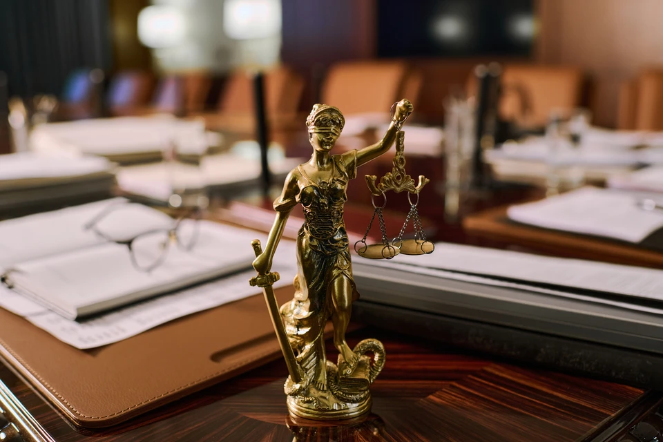 Un homme d'affaires en costume gris et cravate rayée examine attentivement des documents avec une loupe dorée tout en tenant un stylo, assis à un bureau avec une pile importante de paperasse